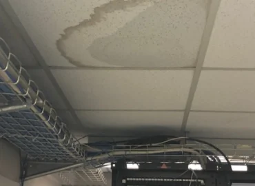 A stained ceiling tile indicates a water leak directly above computer equipment racks in an office setting.